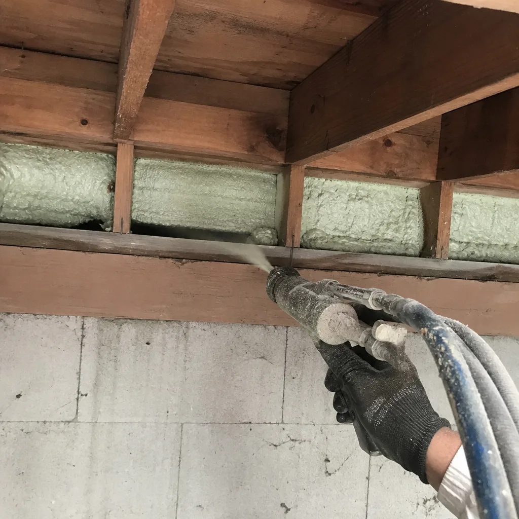 Worker applying professional spray foam insulation to wooden floor joists